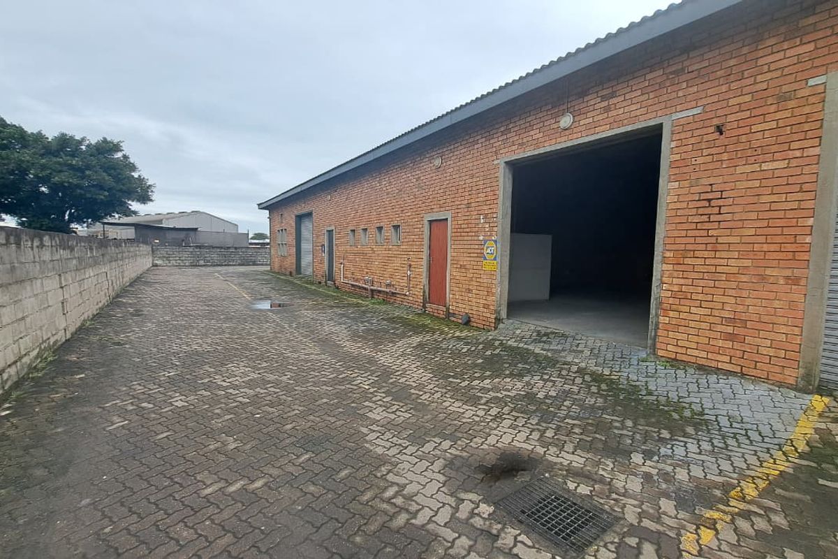 Rear exterior view of an industrial property featuring face brick construction, paved yard space, and multiple roller shutter access points.