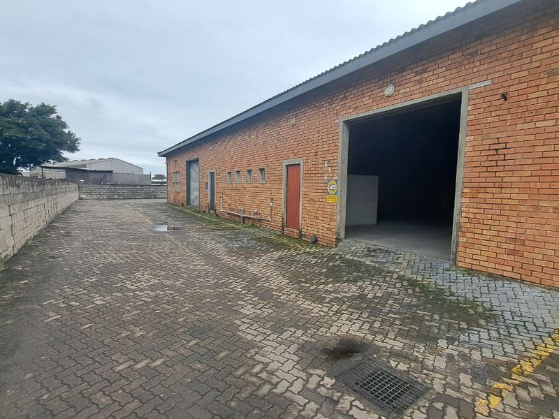 Rear exterior view of an industrial property featuring face brick construction, paved yard space, and multiple roller shutter access points.