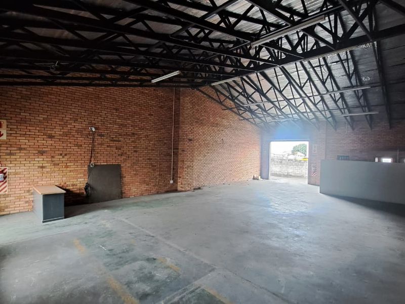 Spacious industrial utility area featuring exposed brick walls, high steel roof trusses, and durable concrete flooring, suitable for storage or workshop use.