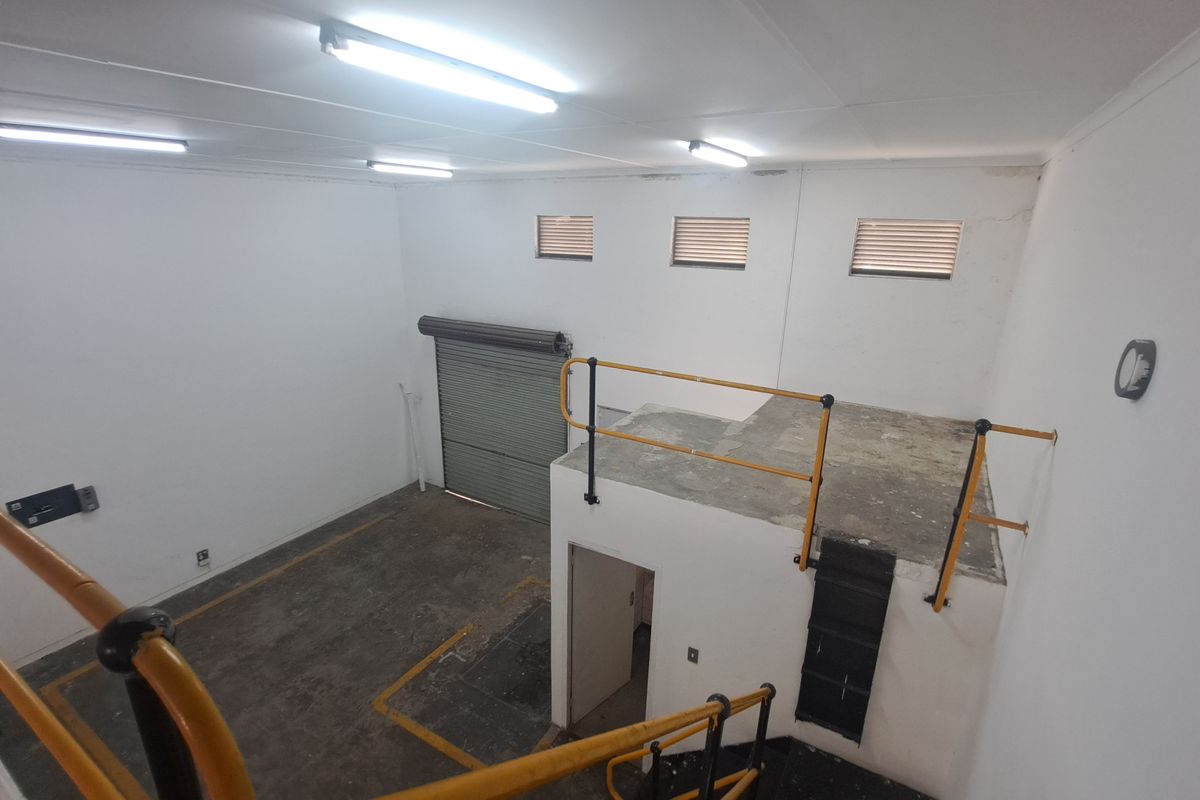 Industrial utility space featuring a mezzanine level with safety railings, concrete flooring, and a large roller shutter door for easy access.