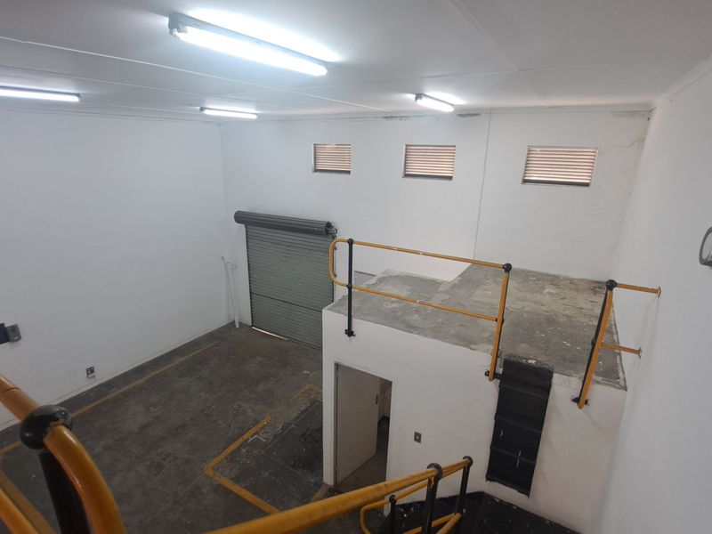 Industrial utility space featuring a mezzanine level with safety railings, concrete flooring, and a large roller shutter door for easy access.