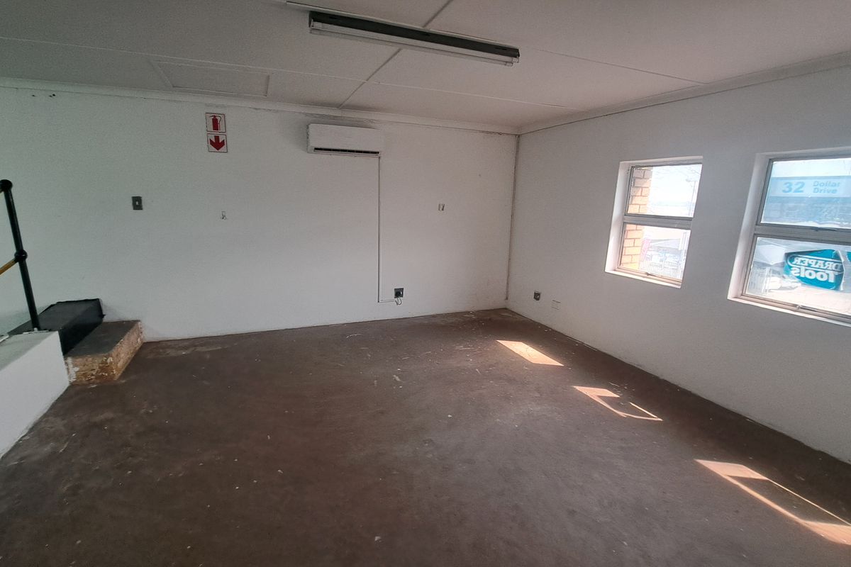 An empty industrial office space featuring concrete flooring, a wall-mounted air conditioning unit, and natural light from two windows.