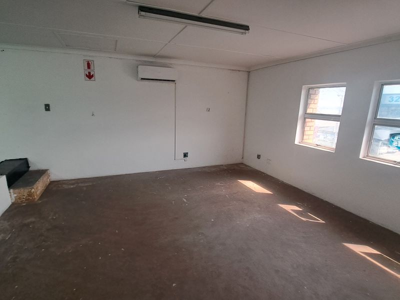 An empty industrial office space featuring concrete flooring, a wall-mounted air conditioning unit, and natural light from two windows.