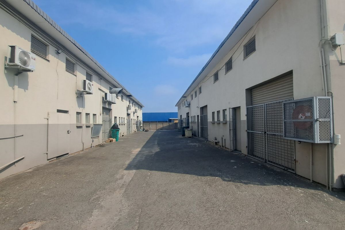 Rear industrial access lane featuring multiple roller shutter doors, security cages, and external air conditioning units between two warehouse structures.