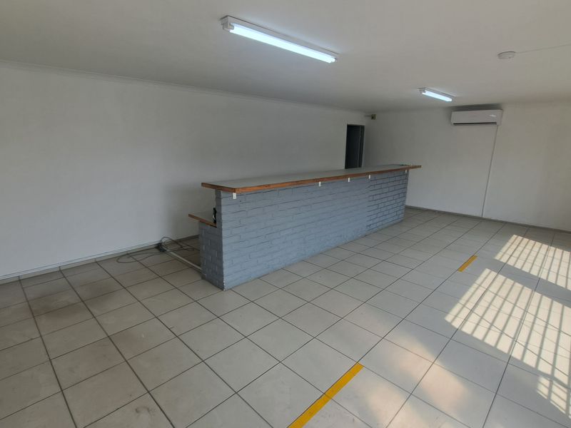An open-plan industrial space featuring a built-in brick bar counter, tiled flooring, air conditioning, and secure window bars.