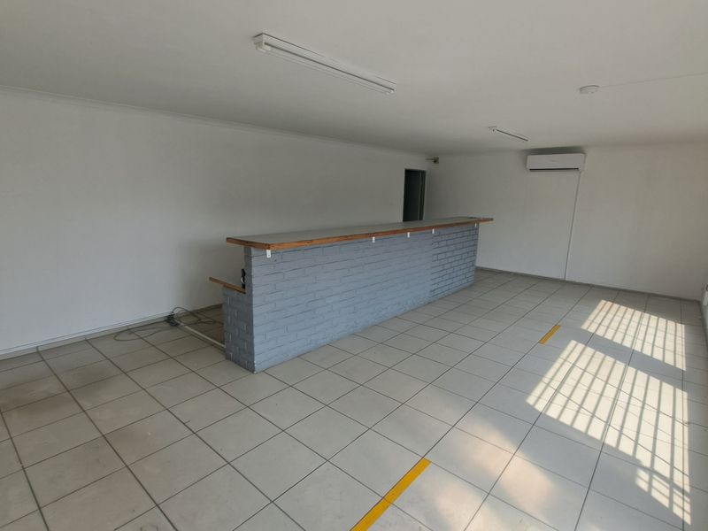 An empty industrial-style space featuring a brick bar counter, tiled flooring, and security-barred windows, suitable for a variety of commercial or office uses.