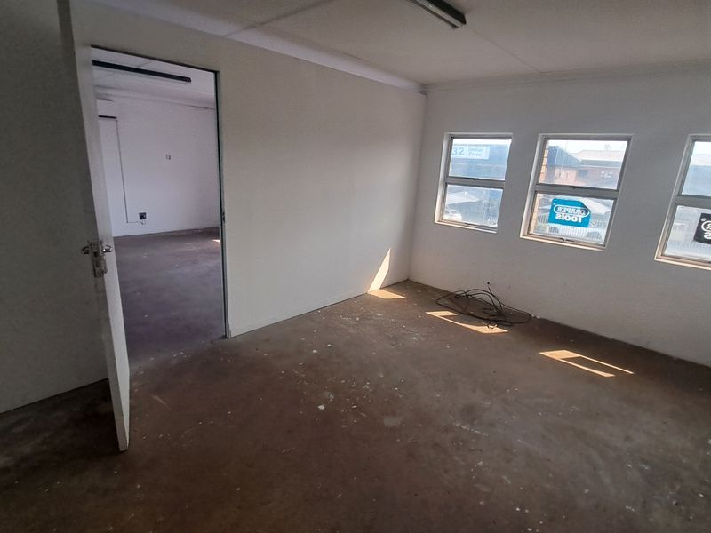 An empty industrial office space featuring concrete flooring, multiple windows providing natural light, and an internal doorway leading to an adjacent room.
