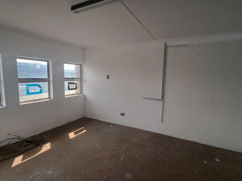 An empty industrial office space featuring white walls, aluminium-framed windows, and basic overhead lighting, suitable for a workshop or administrative area.