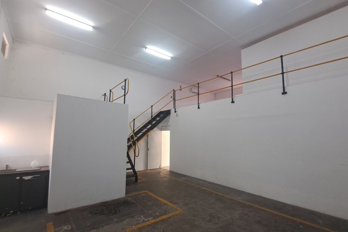 Industrial utility space featuring a mezzanine level with metal staircase, safety railings, concrete flooring, and a small kitchenette area.