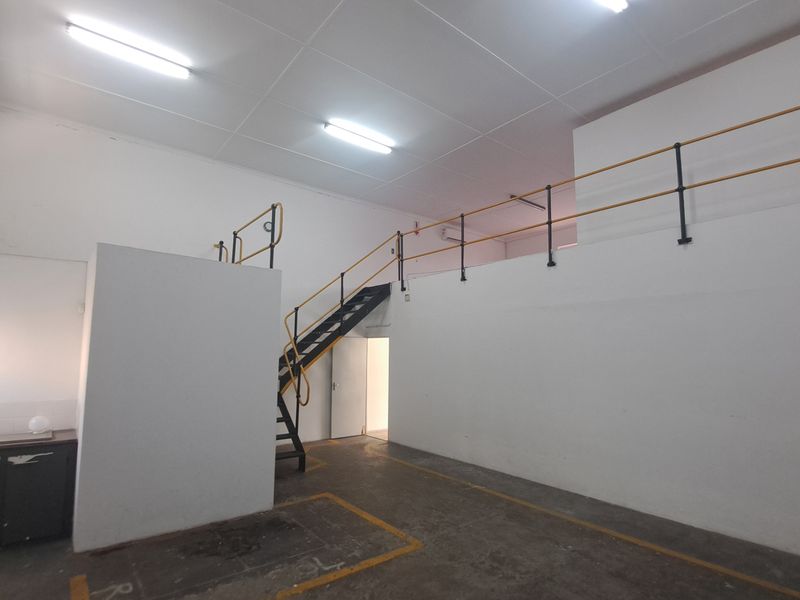 Industrial utility space featuring a mezzanine level with metal staircase, safety railings, concrete flooring, and a small kitchenette area.
