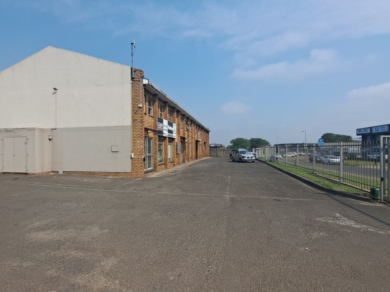 Industrial property exterior featuring a large asphalt parking area, brick facade, and secure perimeter fencing.