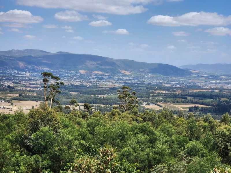 A scenic elevated landscape view overlooking the surrounding valley, farmland, and distant mountain range under a clear blue sky.
