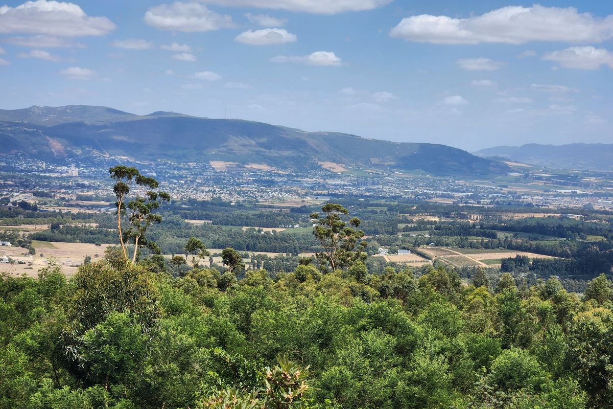 A scenic elevated landscape view overlooking the surrounding valley, farmland, and distant mountain range under a clear blue sky.