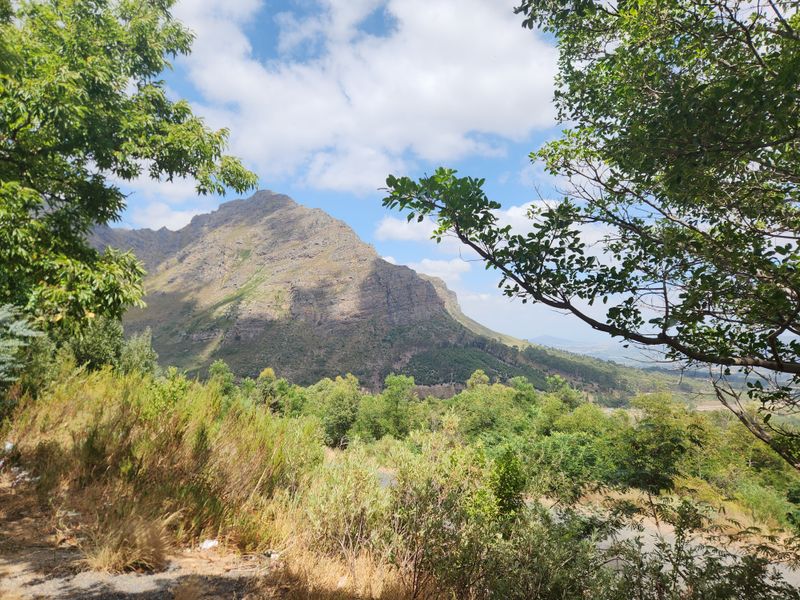 A scenic landscape view of a prominent mountain range surrounded by lush greenery and natural vegetation.