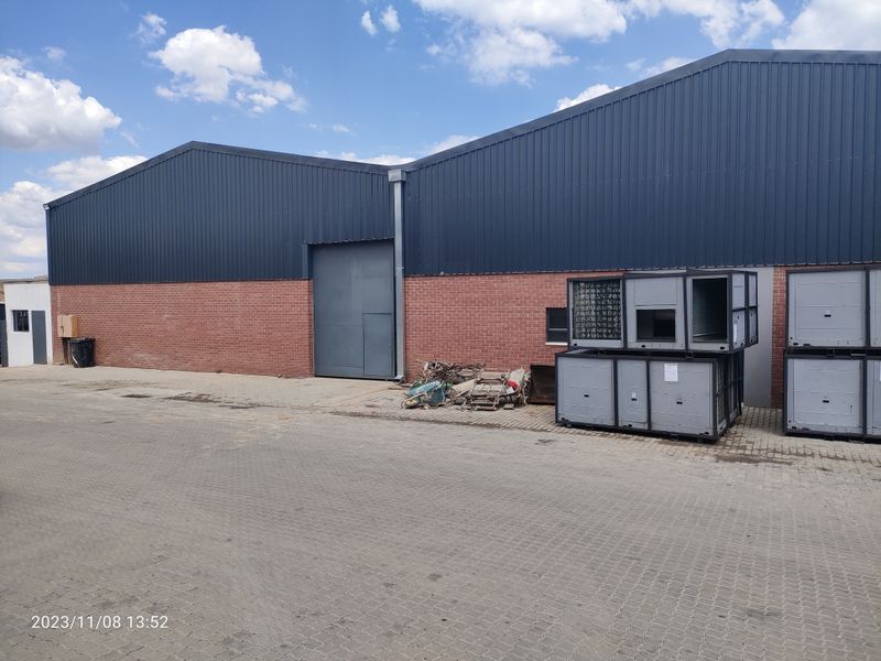 Industrial warehouse exterior featuring a combination of brick and metal cladding with a large sliding access door and paved yard area.