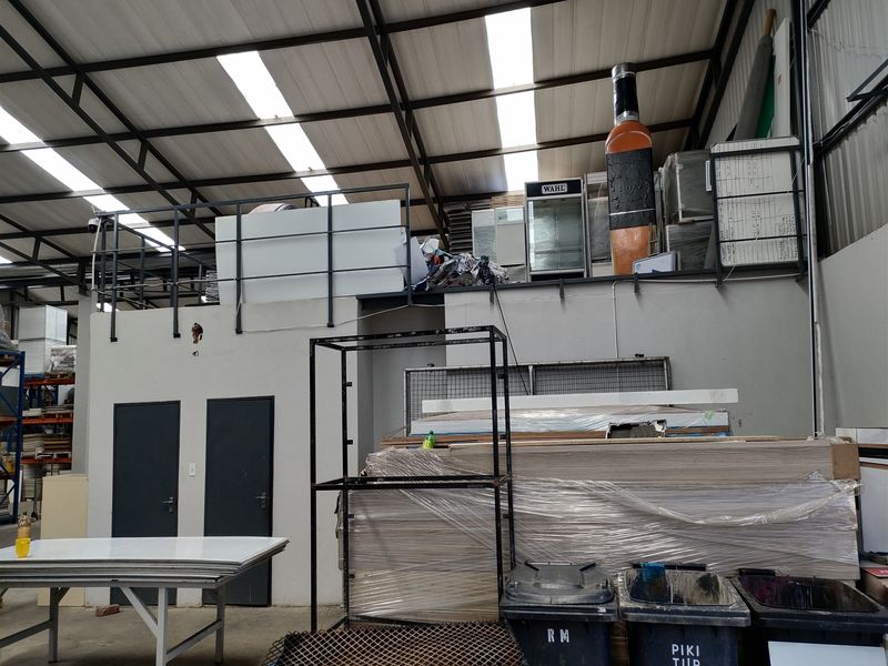 Industrial utility space featuring a mezzanine level, high-clearance metal roof structure with integrated skylights, and functional access doors.