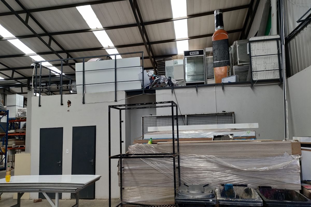 Industrial utility space featuring a mezzanine level, high-clearance metal roof structure with integrated skylights, and functional access doors.