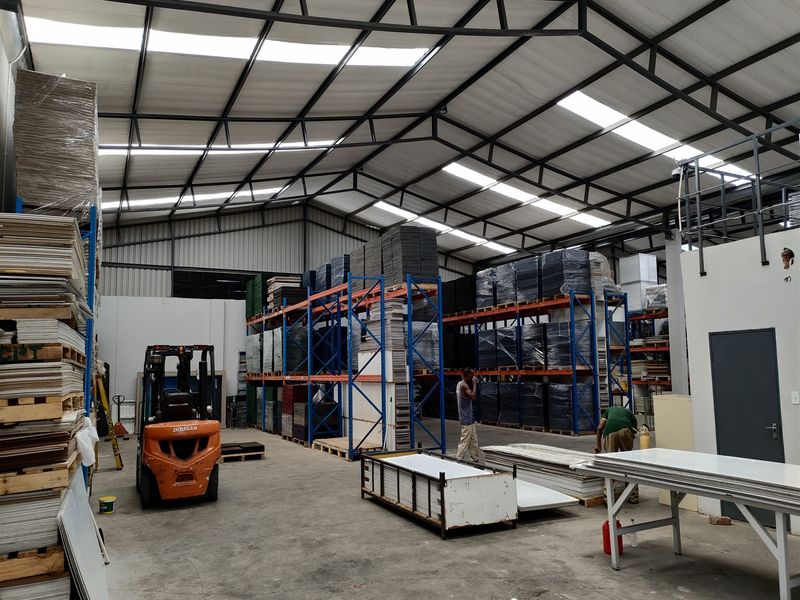 Spacious industrial warehouse featuring high steel truss ceilings, integrated skylights, concrete flooring, and extensive heavy-duty racking systems for storage.