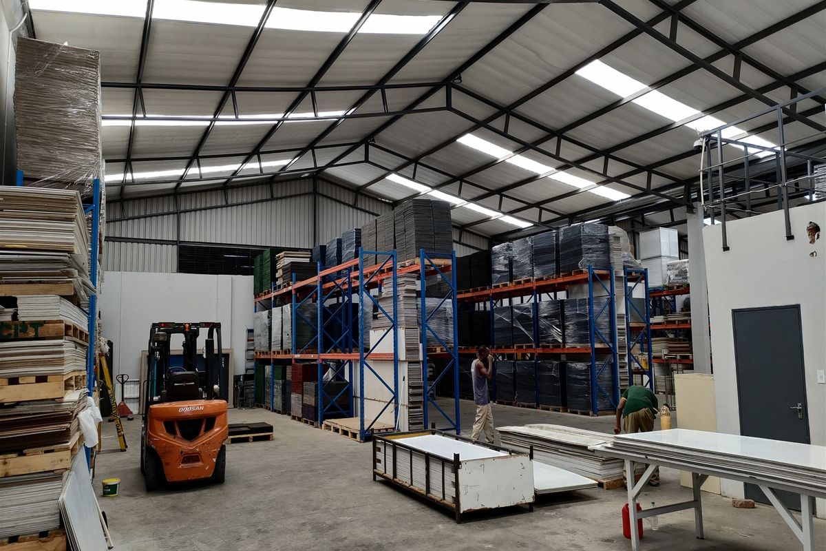Spacious industrial warehouse featuring high steel truss ceilings, integrated skylights, concrete flooring, and extensive heavy-duty racking systems for storage.