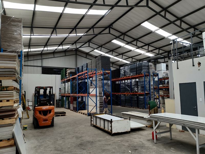 Spacious industrial warehouse featuring high steel truss ceilings with integrated skylights, concrete flooring, and extensive heavy-duty racking systems for storage.