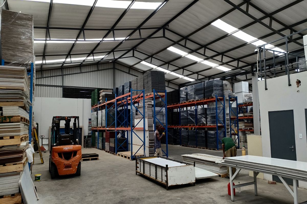 Spacious industrial warehouse featuring high steel truss ceilings with integrated skylights, concrete flooring, and extensive heavy-duty racking systems for storage.