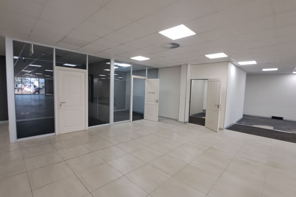 Spacious open-plan office area featuring glass partitions, recessed LED lighting, and tiled flooring, offering a clean and professional workspace environment.