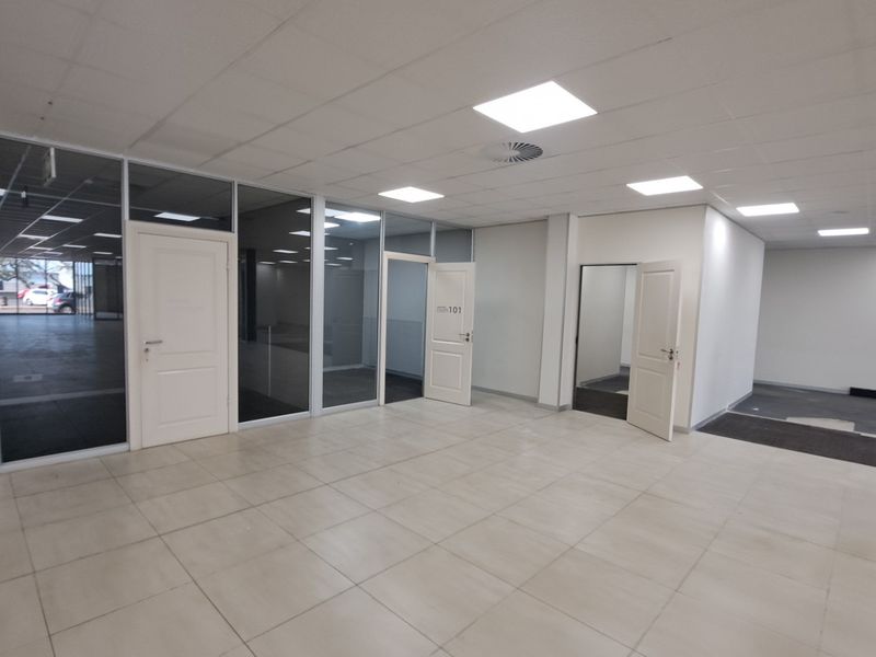 Spacious open-plan office area featuring glass partitions, recessed LED lighting, and tiled flooring, offering a clean and professional workspace environment.