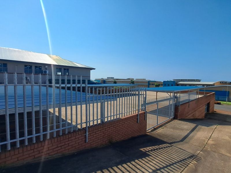 Exterior view of the office property featuring a paved parking area, metal carport structures, and secure perimeter fencing with a brick boundary wall.