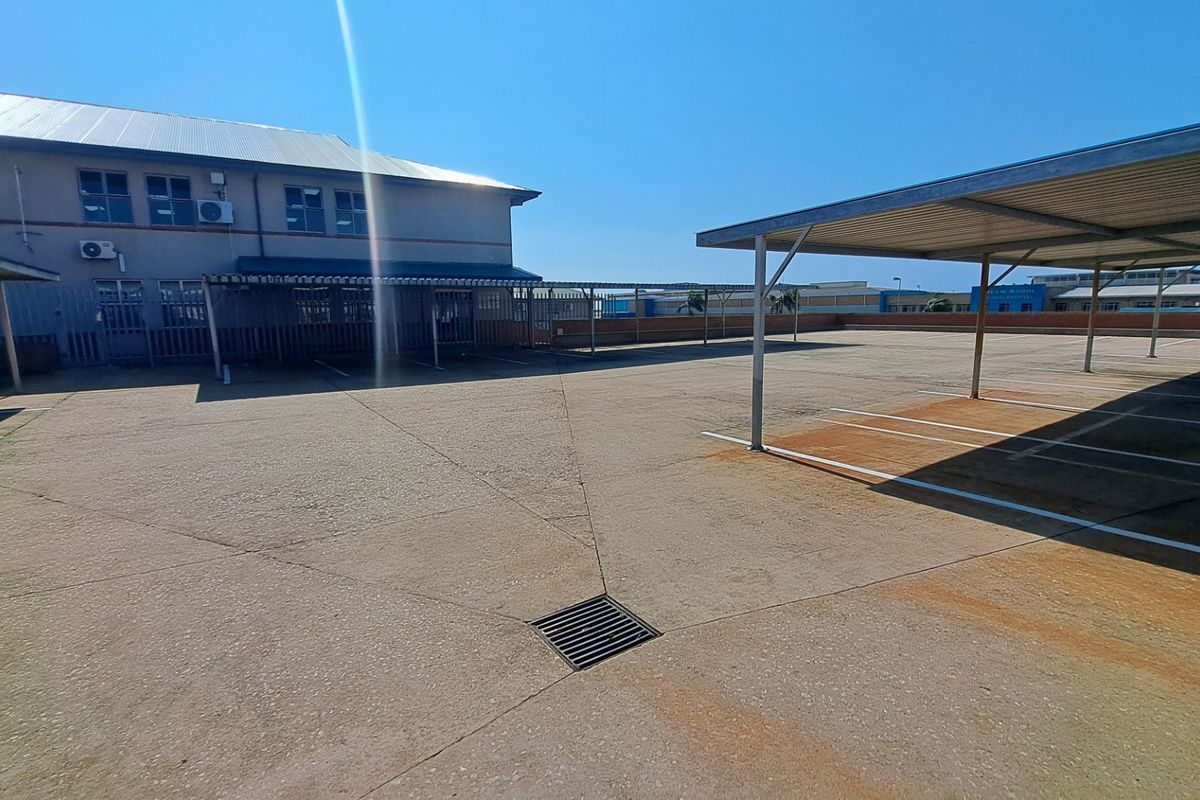 Exterior view of a paved office parking area featuring multiple metal carport structures and building access points.