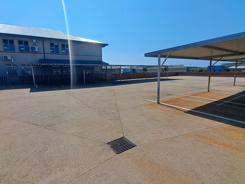 Exterior view of a paved office parking area featuring multiple metal carport structures and building access points.