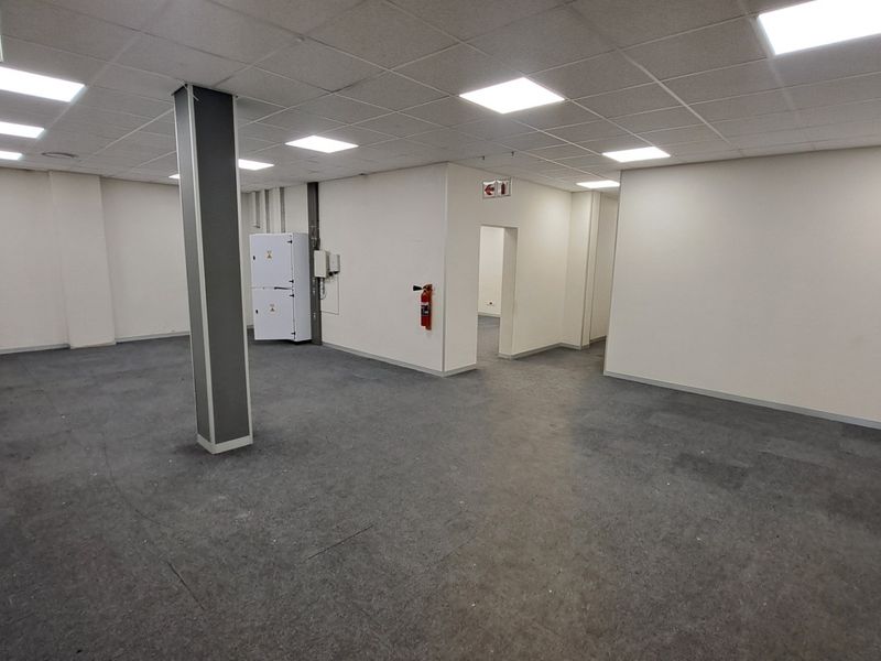 A spacious, open-plan office area featuring a suspended ceiling with recessed lighting, carpeted flooring, and a central structural column.