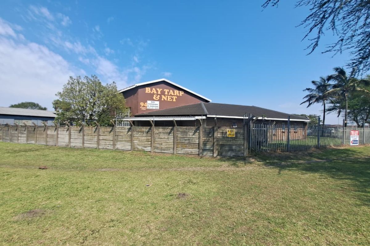 Front exterior view of an industrial property featuring a tiled roof building, secured by a precast concrete wall and razor wire fencing.