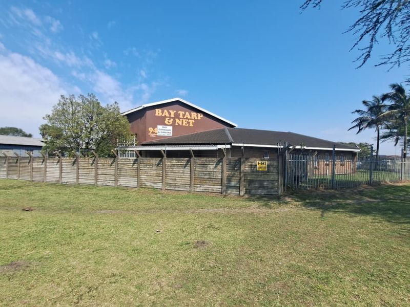 Front exterior view of an industrial property featuring a tiled roof building, secured by a precast concrete wall and razor wire fencing.