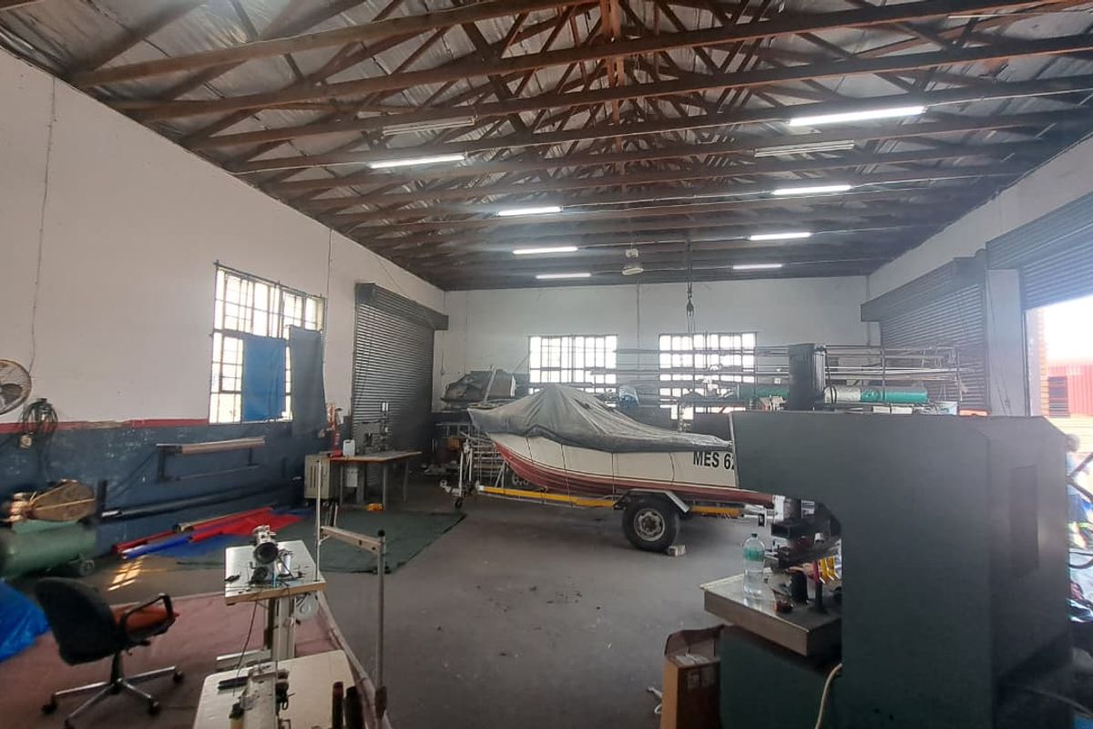 Spacious industrial utility area featuring exposed timber roof trusses, high ceilings, roller shutter doors, and large steel-framed windows suitable for workshop or storage use.