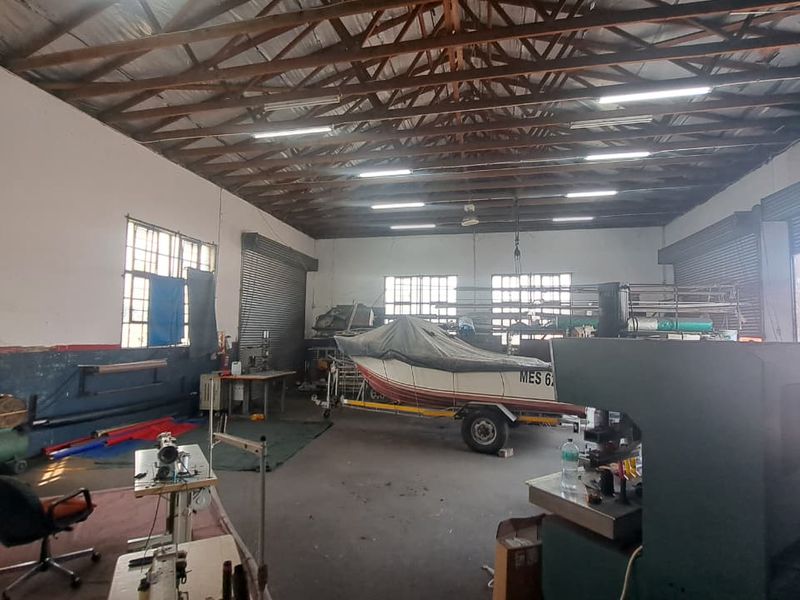 Spacious industrial utility area featuring exposed timber roof trusses, high ceilings, roller shutter doors, and large steel-framed windows suitable for workshop or storage use.