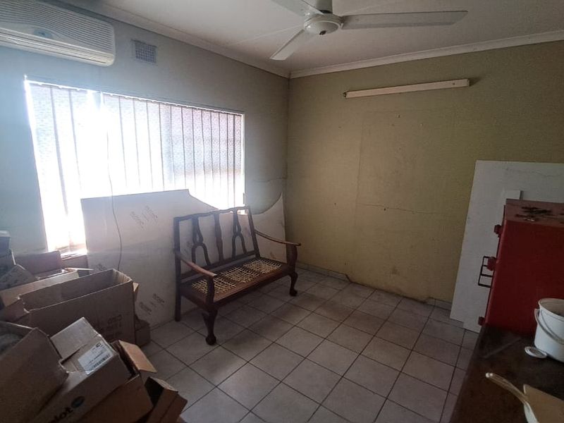 An office space featuring tiled flooring, a ceiling fan, and a wall-mounted air conditioning unit, currently used for storage.