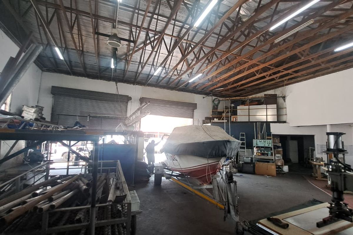 Spacious industrial utility area featuring high ceilings with exposed timber trusses, concrete flooring, and large roller shutter doors for vehicle or equipment access.