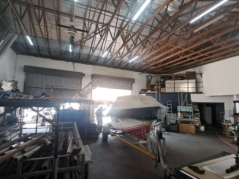 Spacious industrial utility area featuring high ceilings with exposed timber trusses, concrete flooring, and large roller shutter doors for vehicle or equipment access.