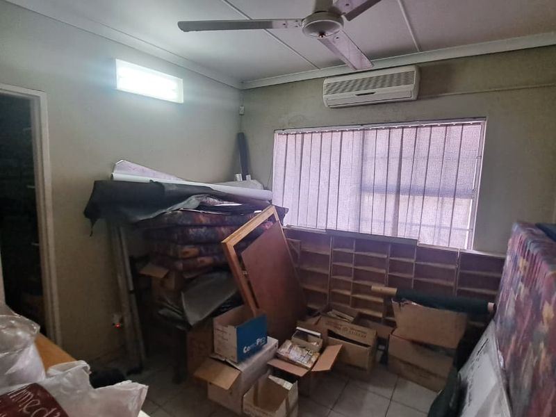 A functional office space featuring tiled flooring, a ceiling fan, and a wall-mounted air conditioning unit, currently used for storage.
