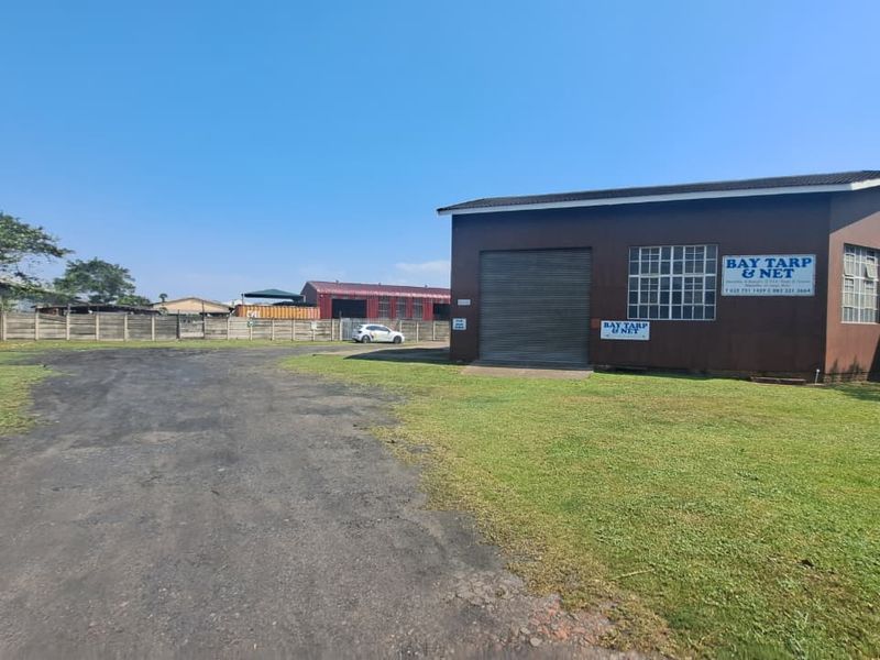 Industrial property featuring a warehouse building with a roller shutter door, steel-framed windows, and a large paved yard area.