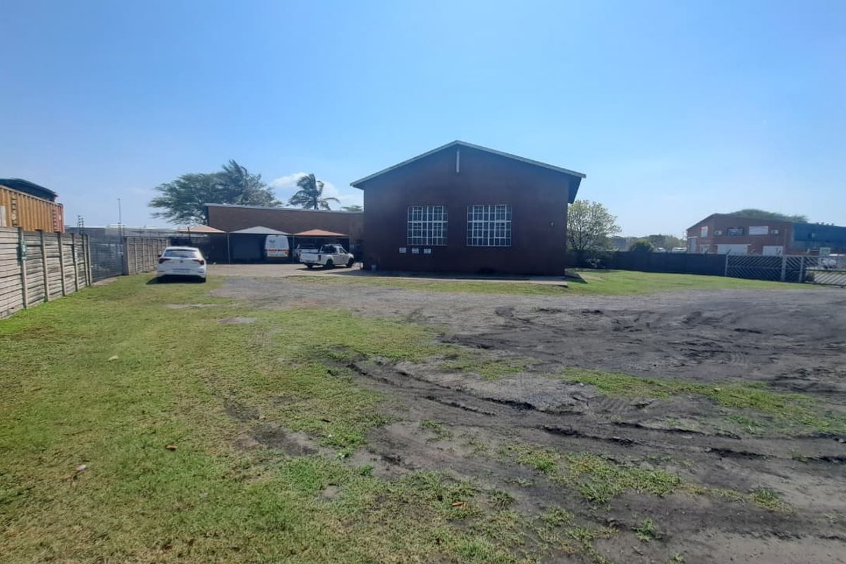 Rear exterior view of an industrial property featuring a brick building, steel-framed windows, and a large open yard area with boundary walling.