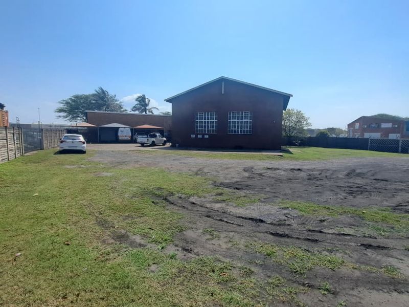 Rear exterior view of an industrial property featuring a brick building, steel-framed windows, and a large open yard area with boundary walling.