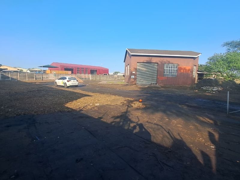 Industrial property exterior featuring a standalone warehouse building with a roller shutter door, set on a large, partially paved yard with boundary fencing.
