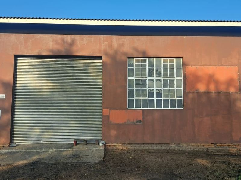 Industrial warehouse exterior featuring a large roller shutter door, steel-framed windows, and a concrete apron entrance.