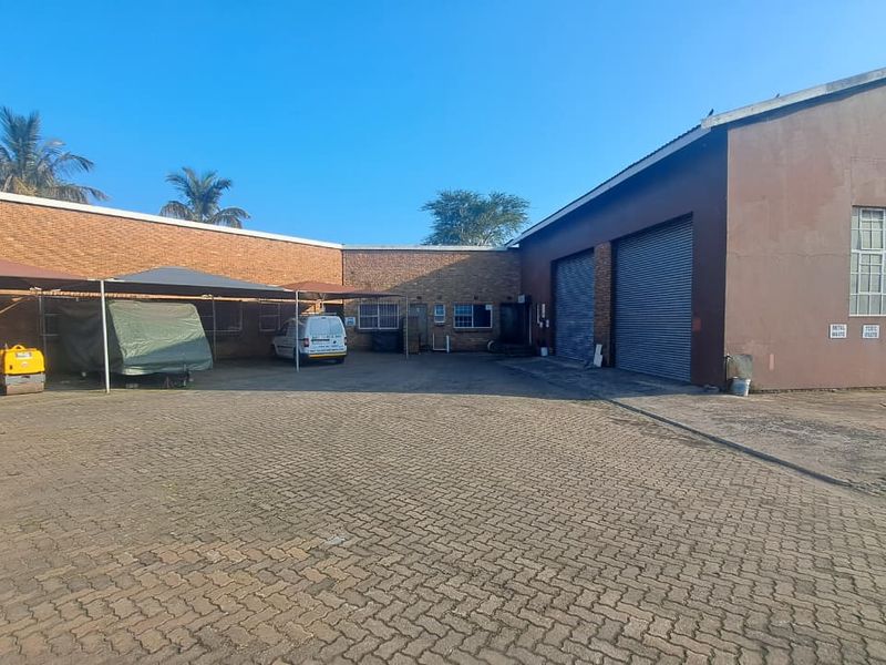 Industrial property exterior featuring a large paved yard, roller shutter doors, and covered parking area.