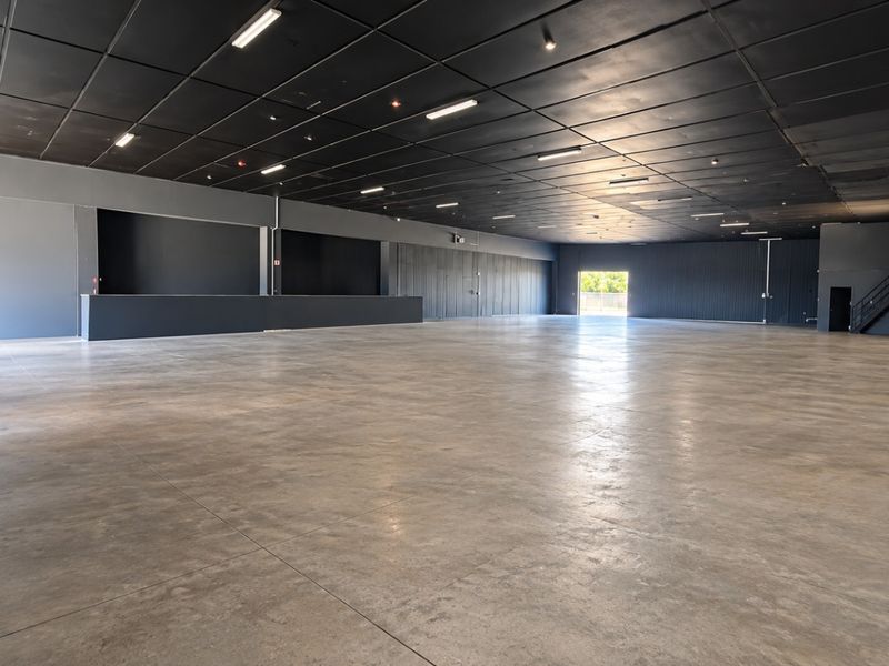 A large, open-plan retail space featuring polished concrete floors, a dark suspended ceiling with recessed lighting, and a built-in service counter.