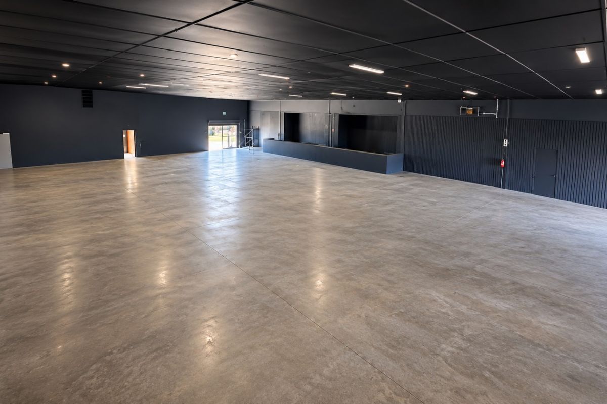 A spacious, open-plan retail or commercial area featuring polished concrete floors, a dark modern ceiling with recessed lighting, and a built-in service counter.