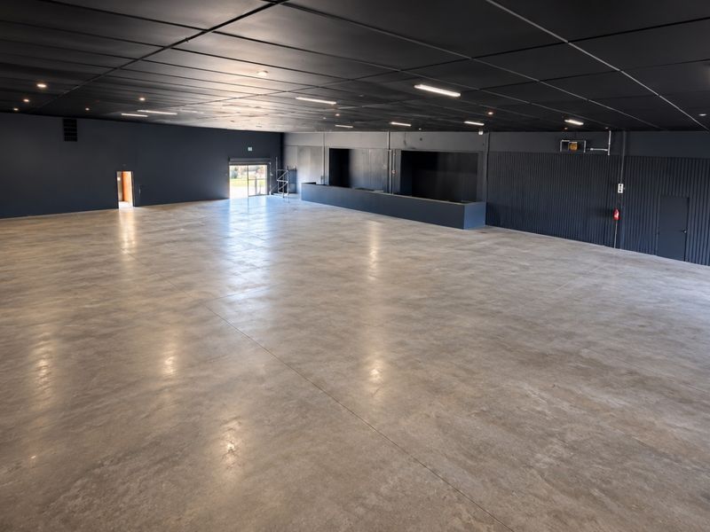 A spacious, open-plan retail or commercial area featuring polished concrete floors, a dark modern ceiling with recessed lighting, and a built-in service counter.