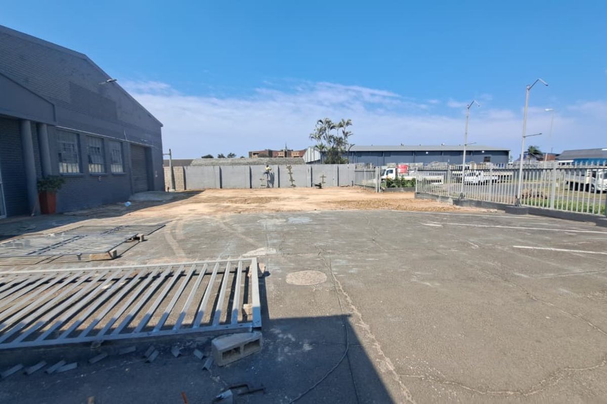 Rear exterior area of the retail property featuring paved parking space, perimeter walling, and metal security fencing.