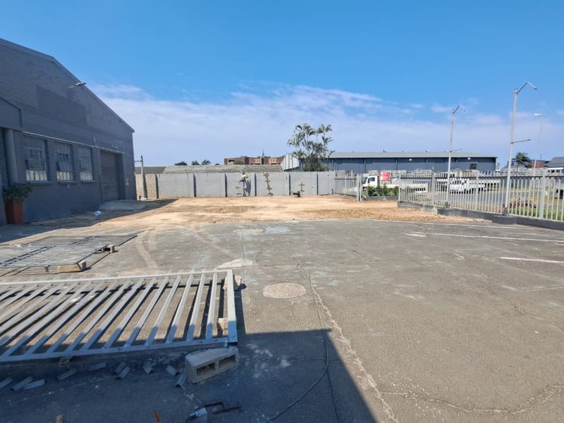 Rear exterior area of the retail property featuring paved parking space, perimeter walling, and metal security fencing.